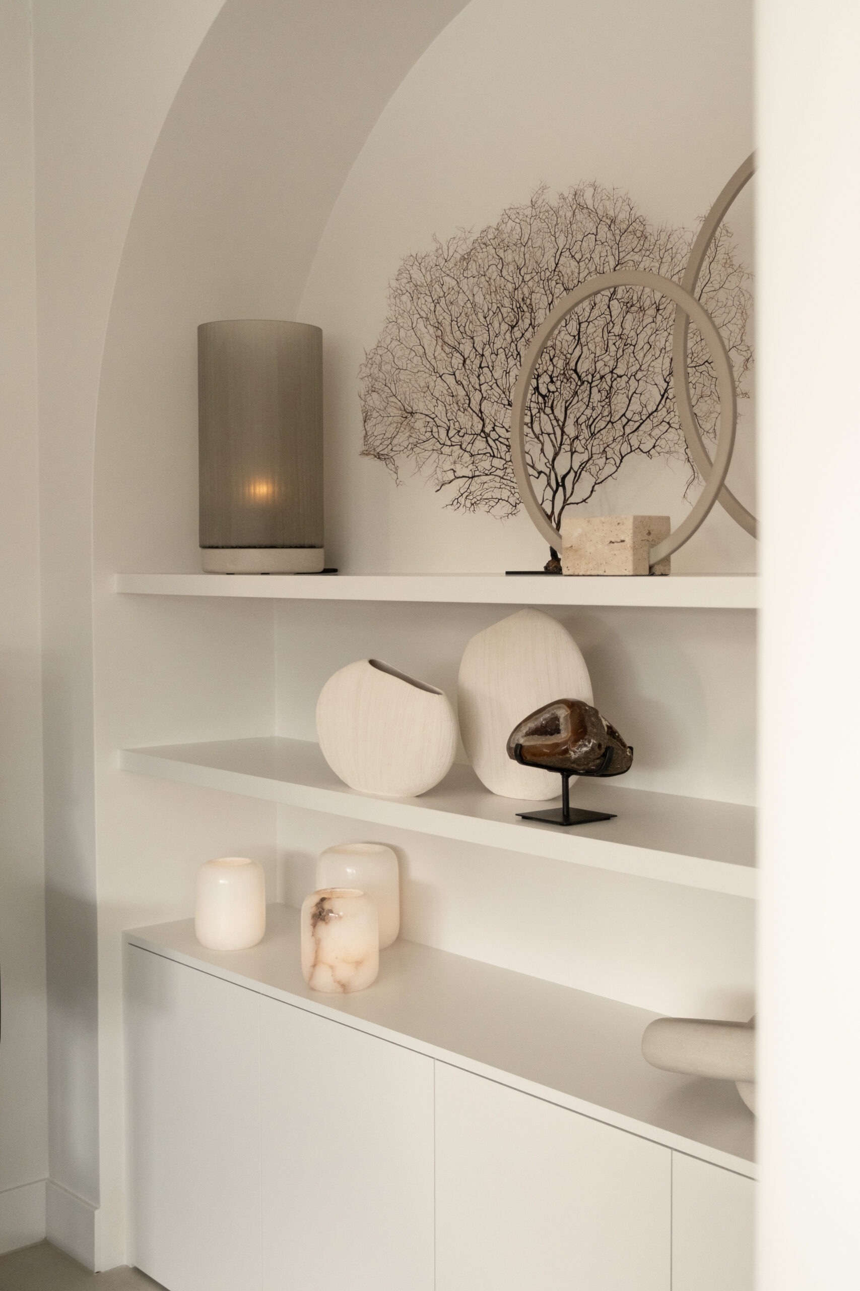 Strakke witte inbouwkast met een elegante boogvormige nis en verfijnde woonaccessoires in woning Uddel door Kardol Hout- en Interieurbouw
