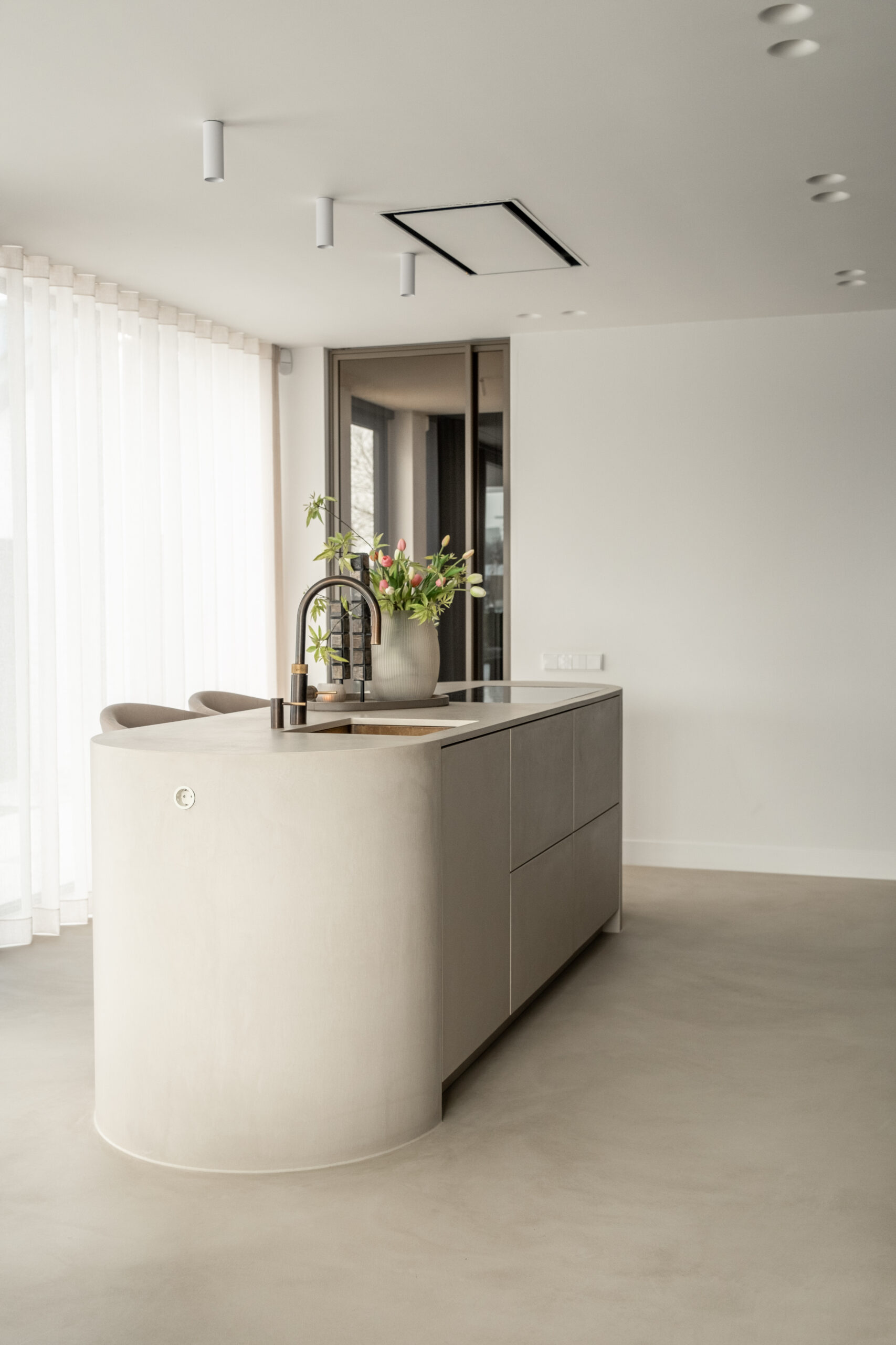 Overzichtsfoto van een vrijstaand beige kookeiland met afgeronde hoeken, bronskleurige kraan en barstoelen in een licht interieur in woning Uddel door Kardol Hout- en Interieurbouw