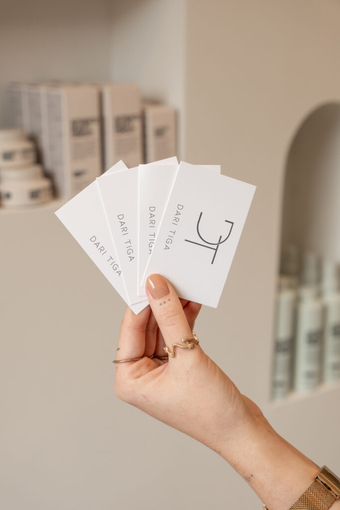 Hand met gouden ringen die een waaier van minimalistische Dari Tiga visitekaartjes vasthoudt in de salon in Putten