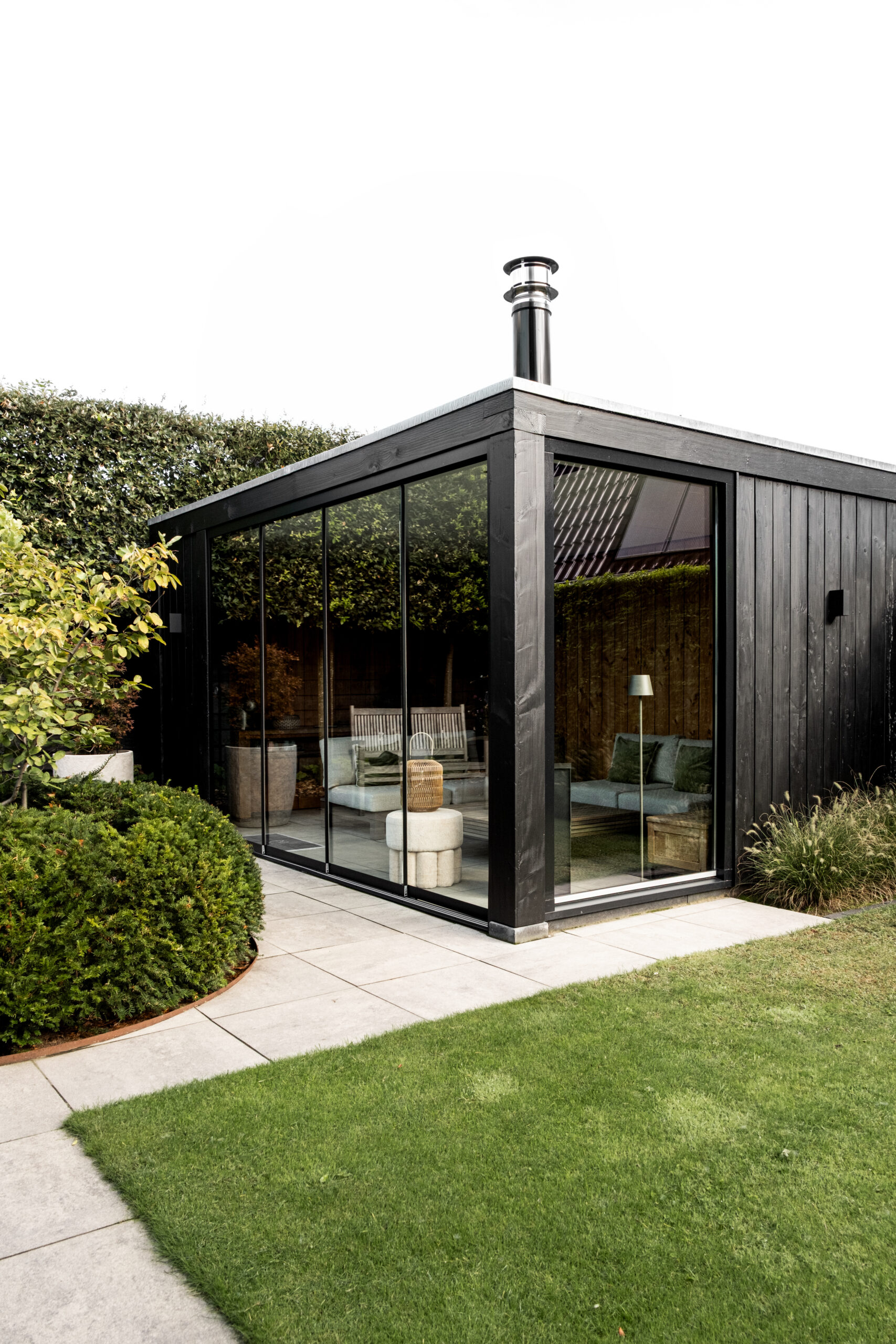 Totaaloverzicht van een luxe zwarte tuinkamer in Lunteren door BG Buitenverblijven met grote glazen wanden, rookkanaal en een strak afgewerkte tuin