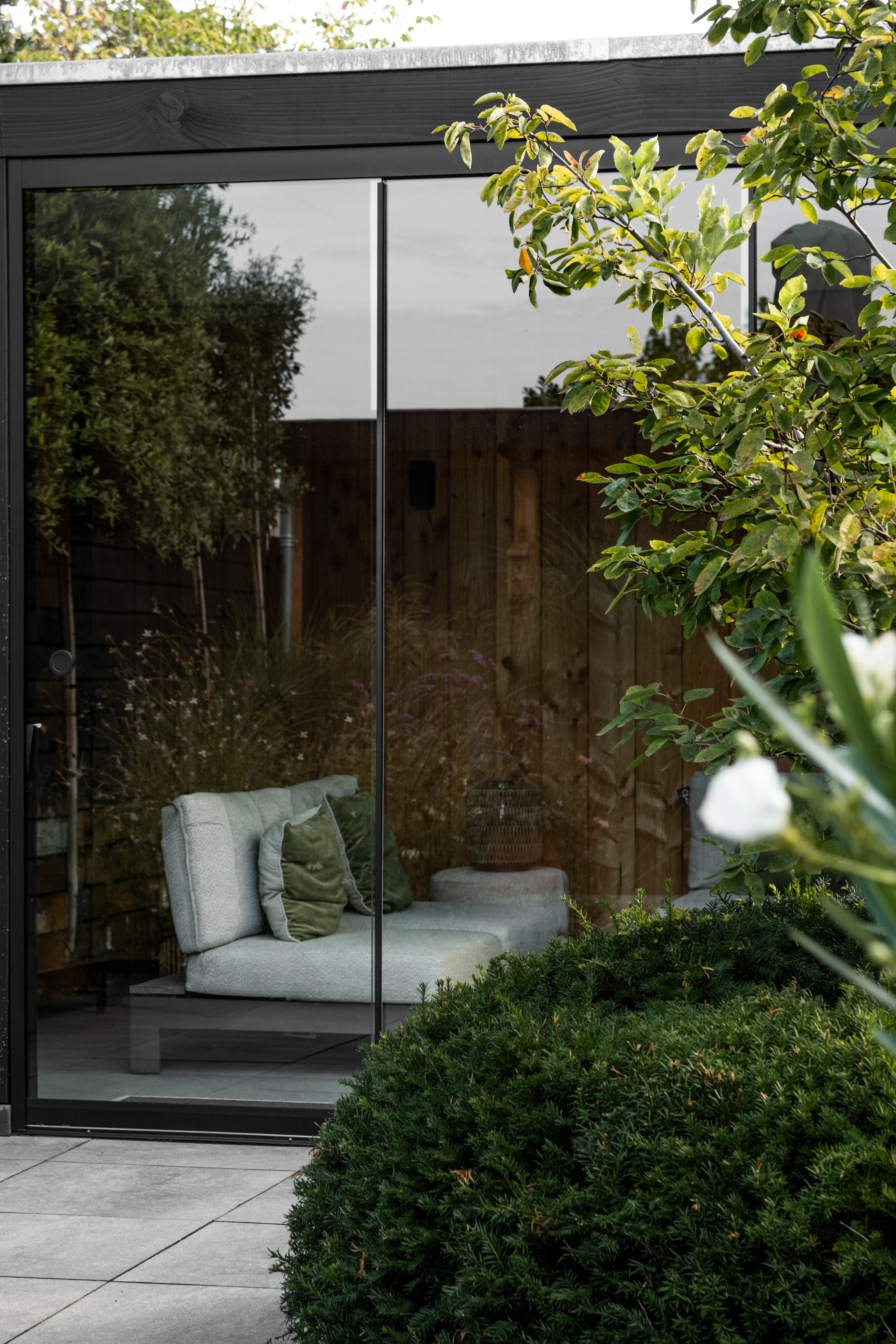 Buitenaanzicht van de moderne tuinkamer in Lunteren door BG Buitenverblijven met zwarte omkadering, grote glazen schuifdeuren en zicht op het lounge-interieur