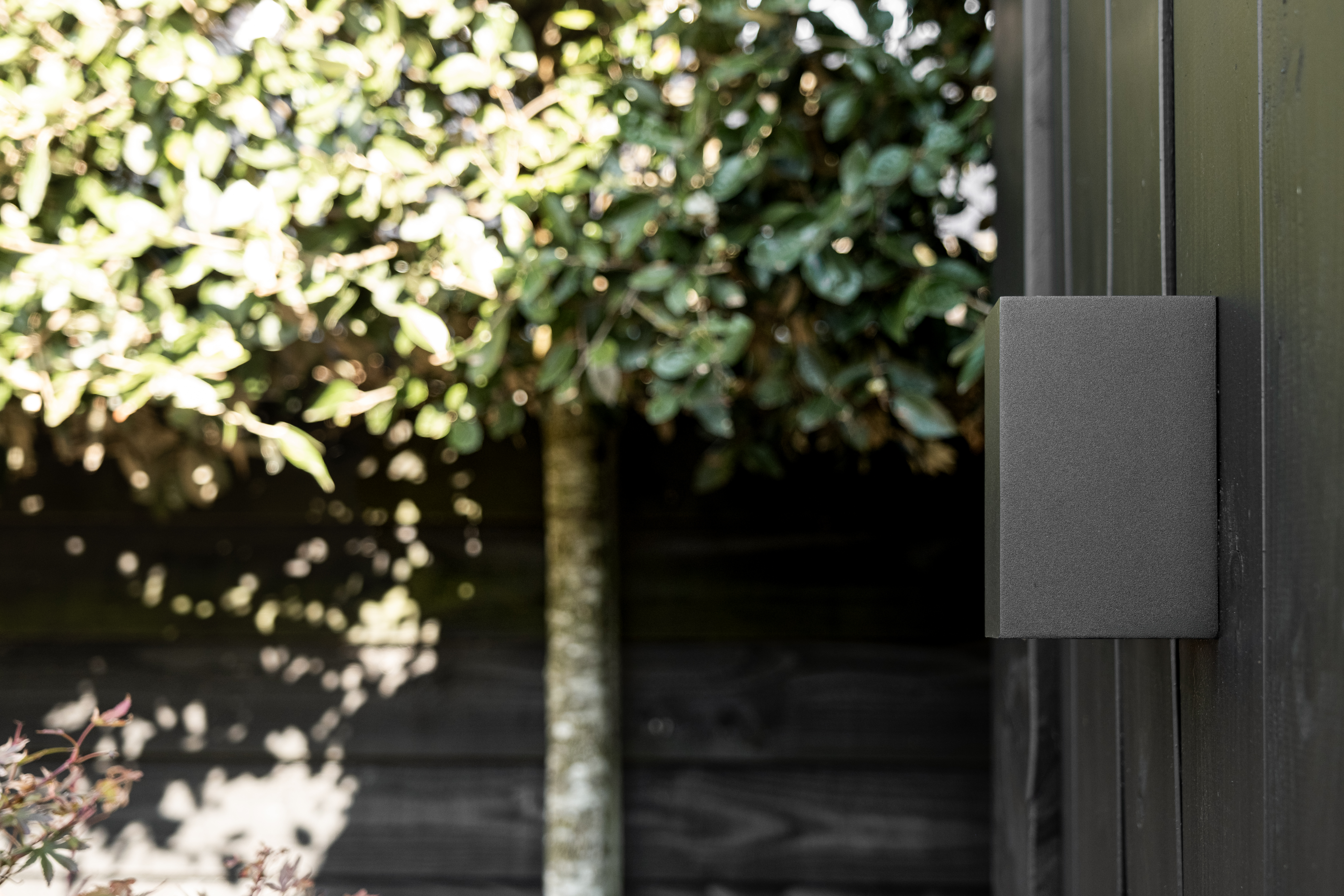 Detailopname van een strakke zwarte buitenlamp gemonteerd op de houten gevelbekleding van de tuinkamer in Lunteren door BG Buitenverblijven
