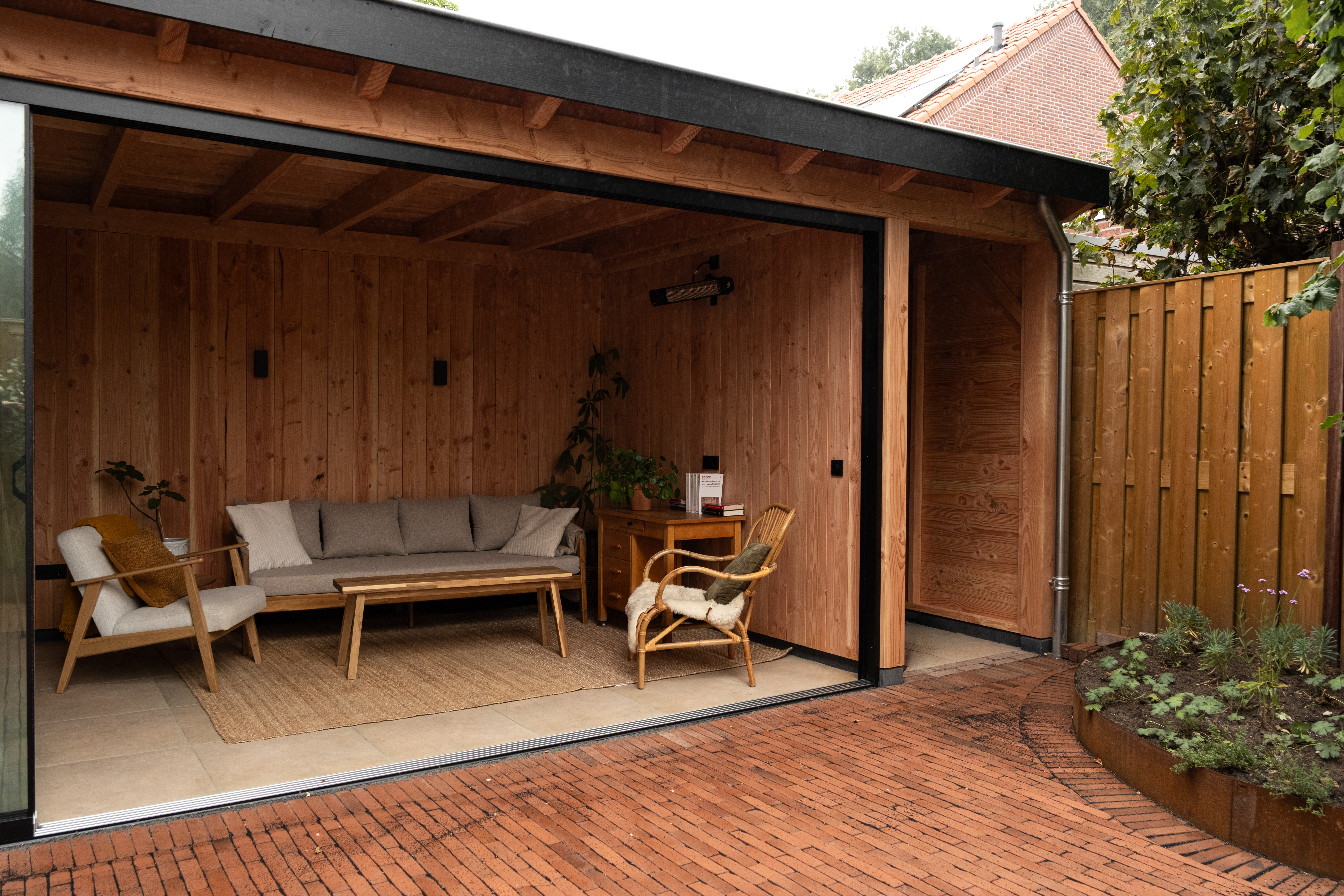 Aanzicht van een luxe houten veranda in Ede met zwarte boeiboord, glazen schuifwand en een gezellige zithoek in de tuin door BG Buitenverblijven