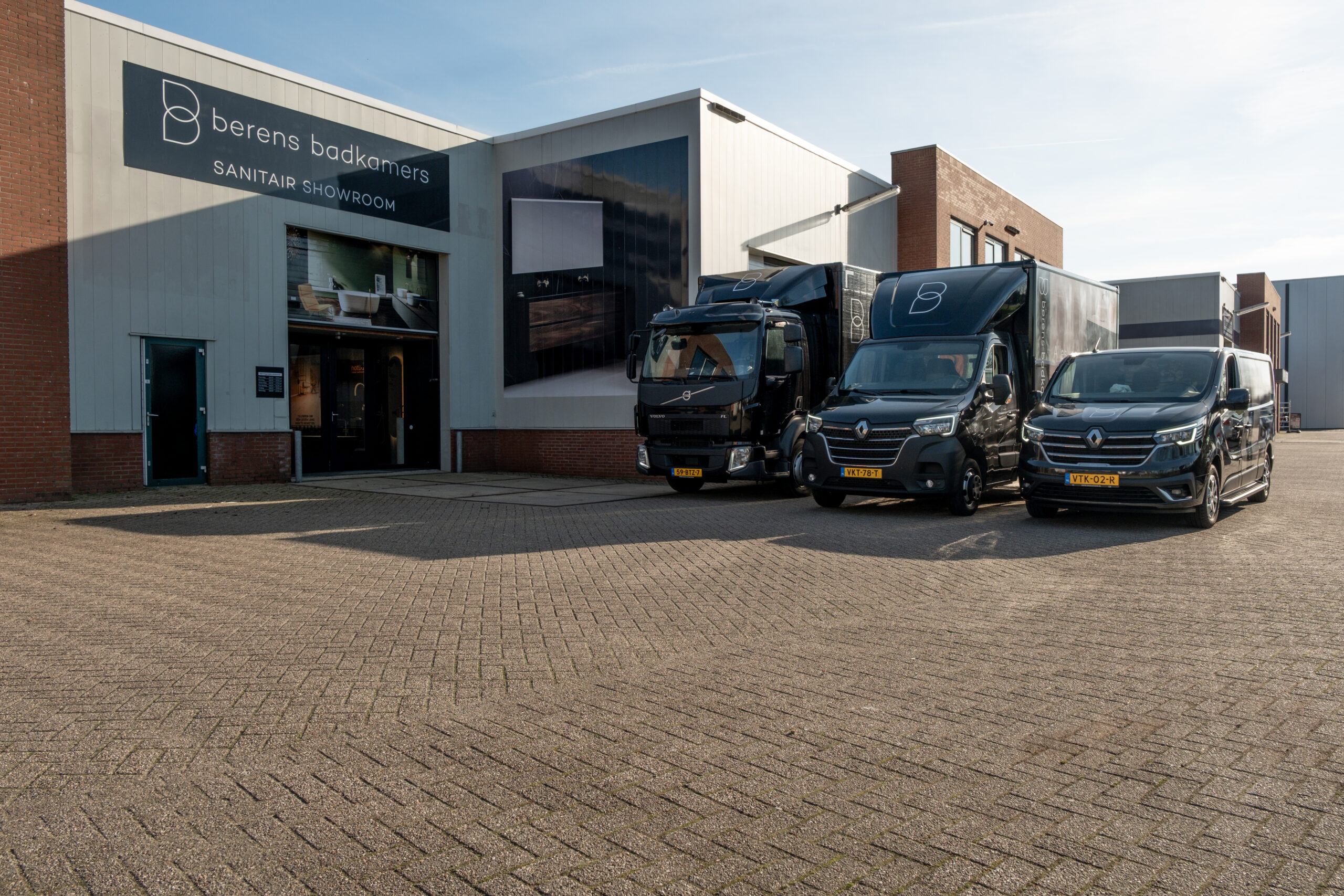 Exterieur van het pand en de showroom van Berends Badkamers in Woerden met zwarte bedrijfswagens voor de deur