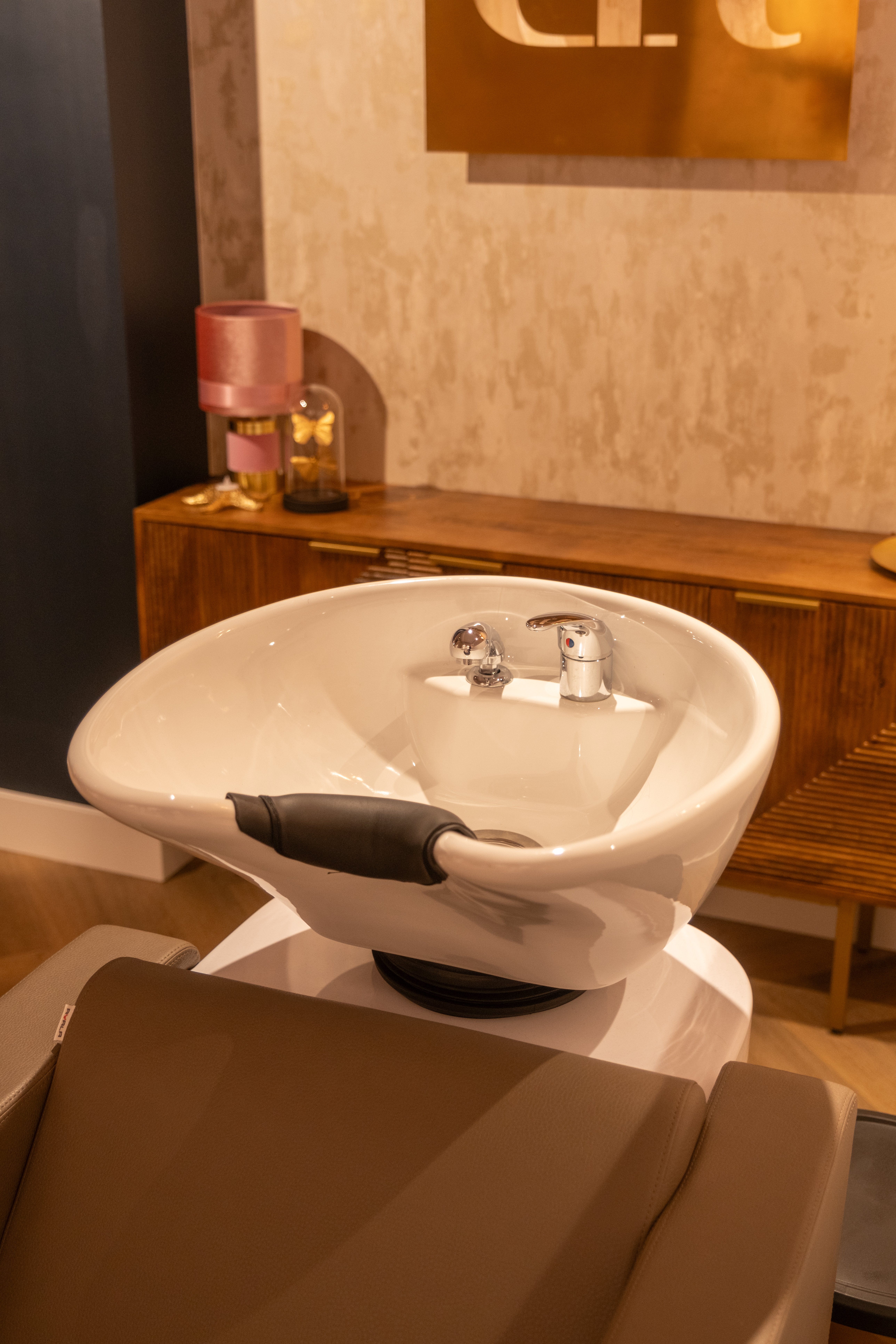 Close-up van de luxe witte wasbak en behandelstoel bij Beauty by Roos Antwerpen met een houten dressoir op de achtergrond