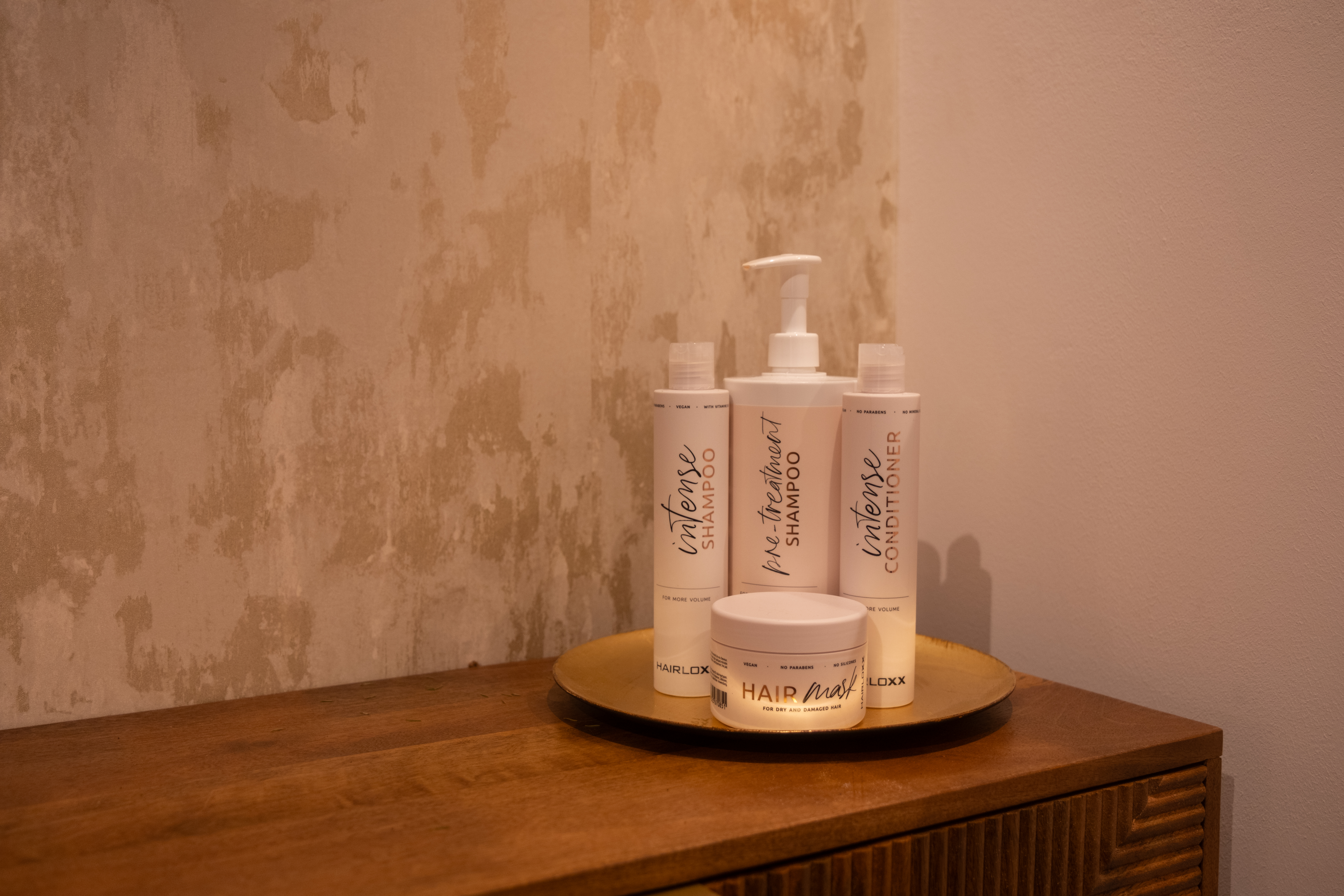 Hairloxx haarverzorgingsproducten op een gouden schaal op een houten dressoir bij Beauty by Roos Antwerpen