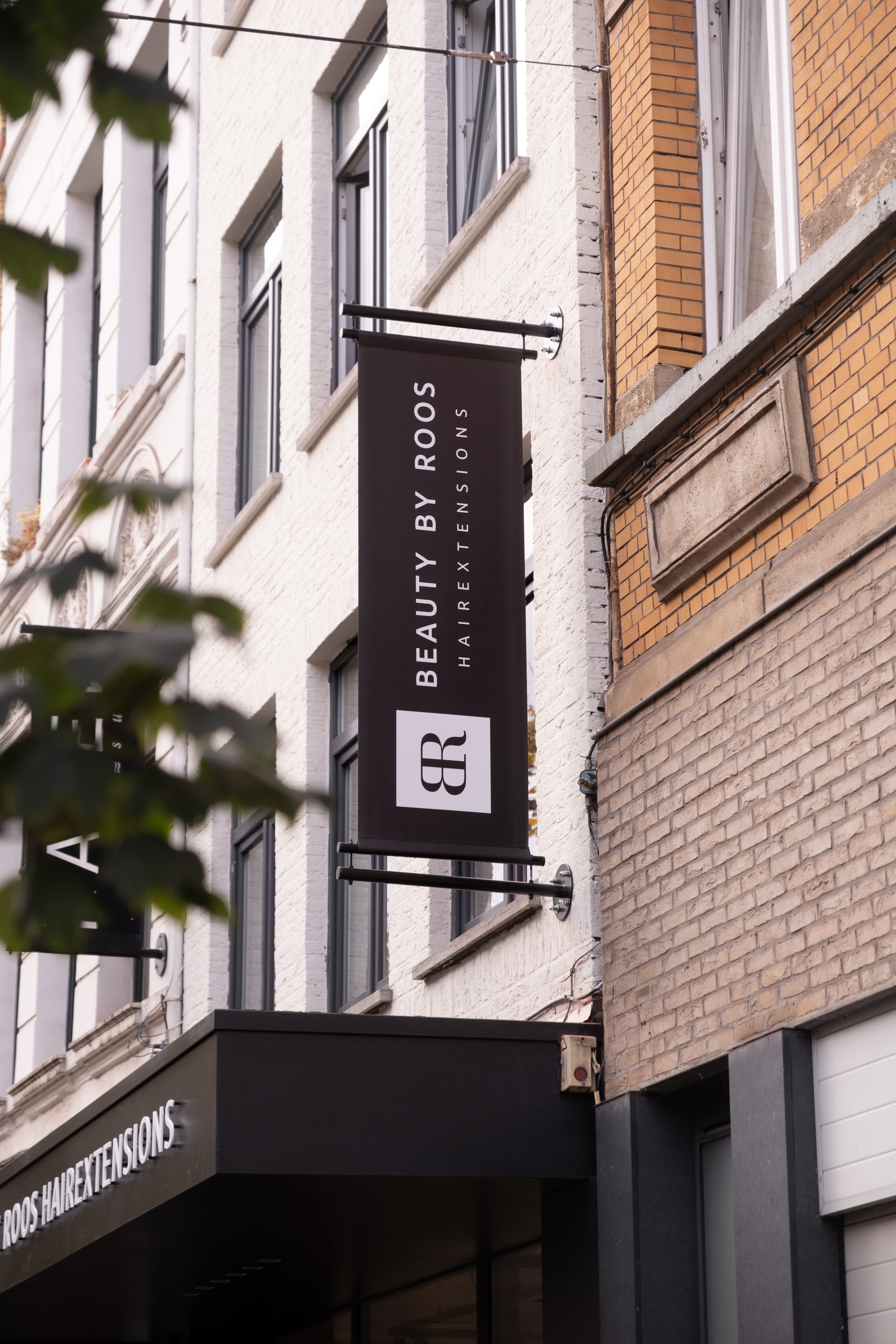 Zwart uithangbord van Beauty by Roos Hairextensions aan de gevel van het pand in Antwerpen