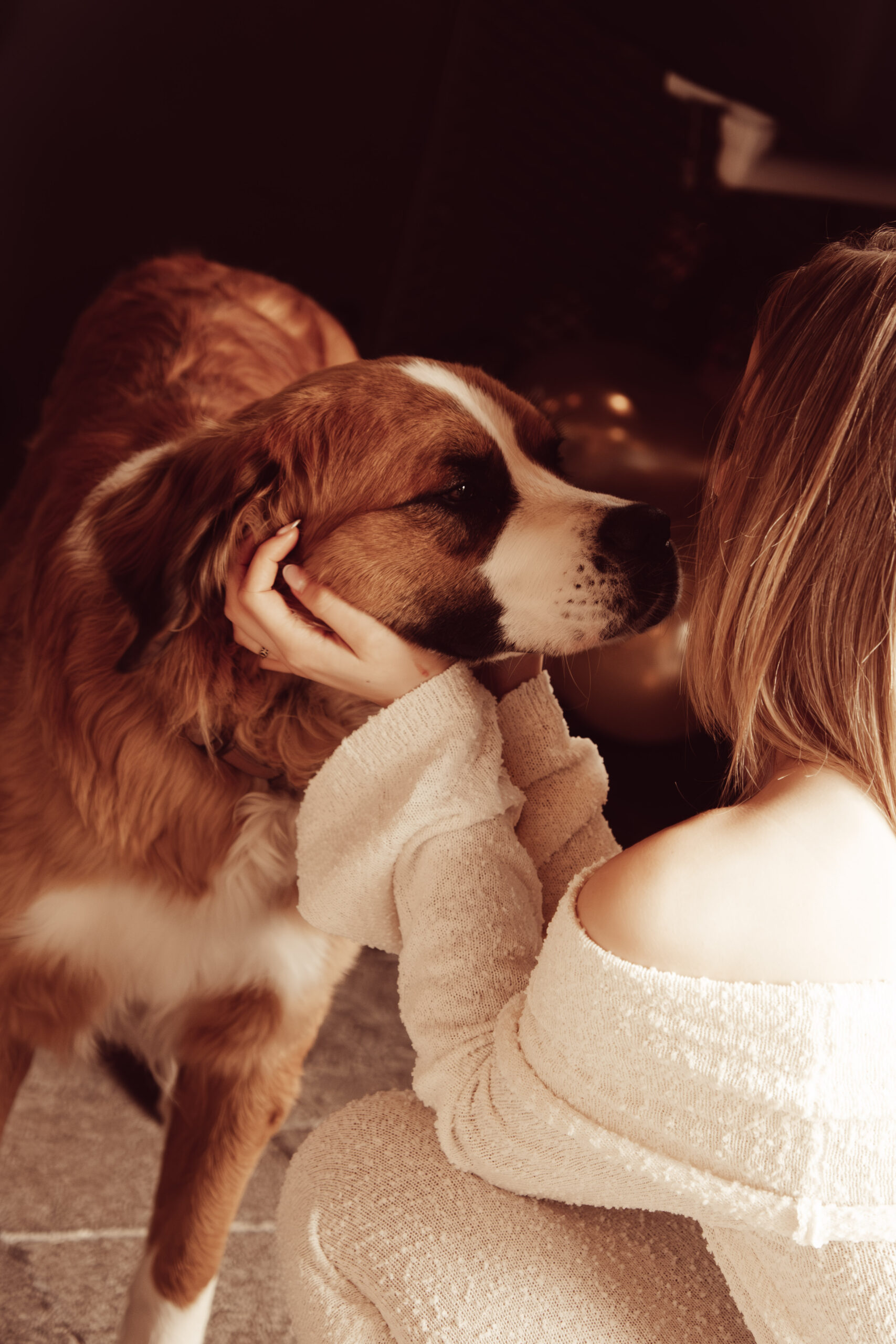 Vrouw in een witte outfit houd liefdevol de kop van een grote Sint-Bernardus hond vast tijdens een feestelijk diner