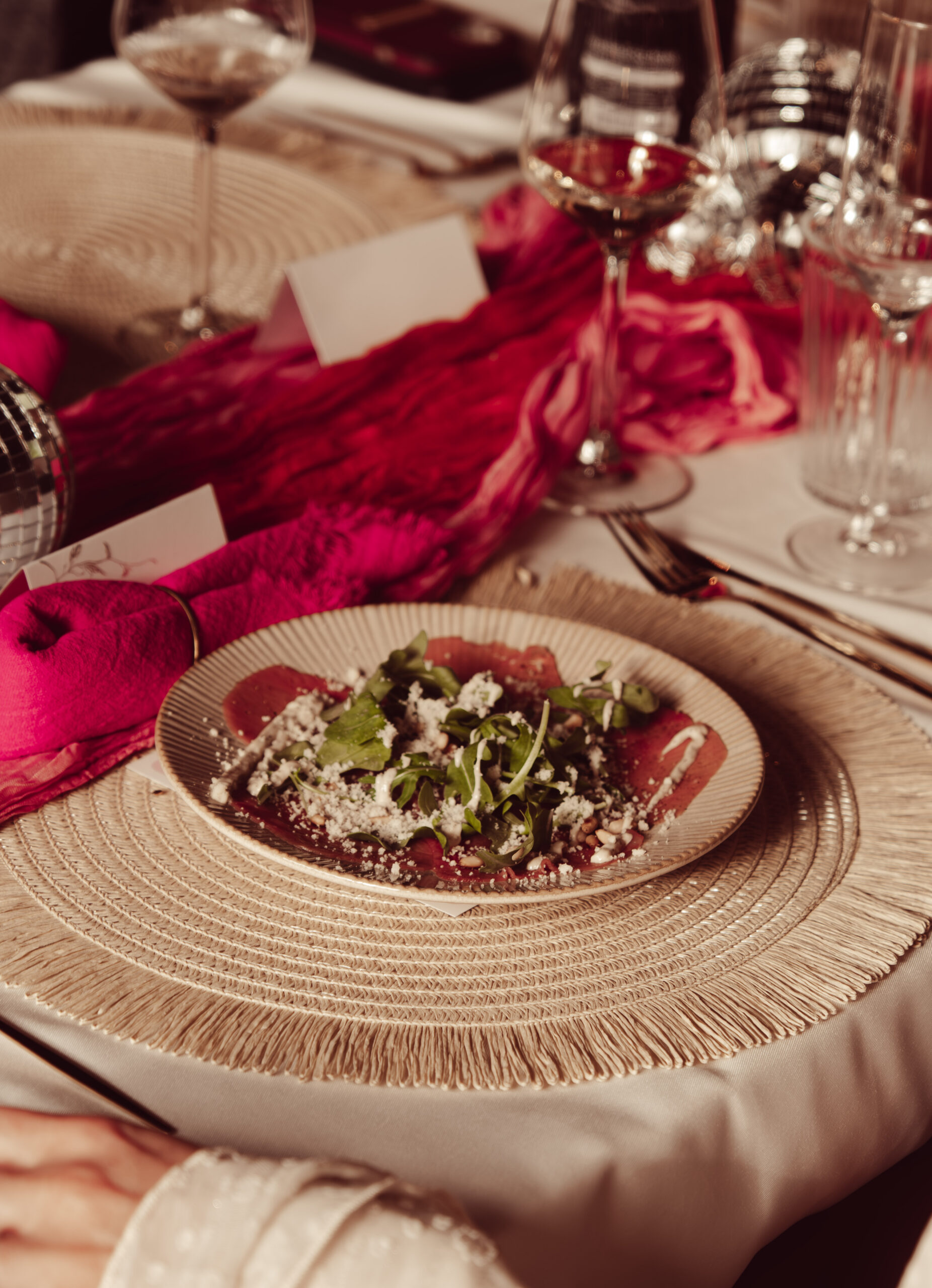 Luxe geserveerde carpaccio met rucola, pijnboompitten en geraspte kaas op een keramisch bord op een sfeervol gedekte dinertafel